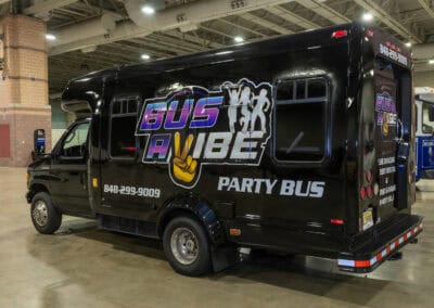 A black Bus A Vibe party bus is parked inside a large indoor area. The bus features the company's logo and contact number on its side.