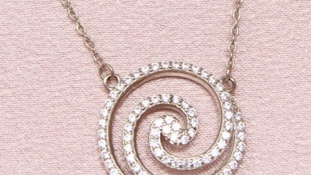 A silver necklace with a pendant featuring a spiral design, encrusted with small diamonds, against a light pink background.