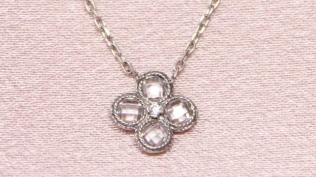 A silver necklace with a pendant shaped like a four-leaf clover adorned with transparent, faceted stones.