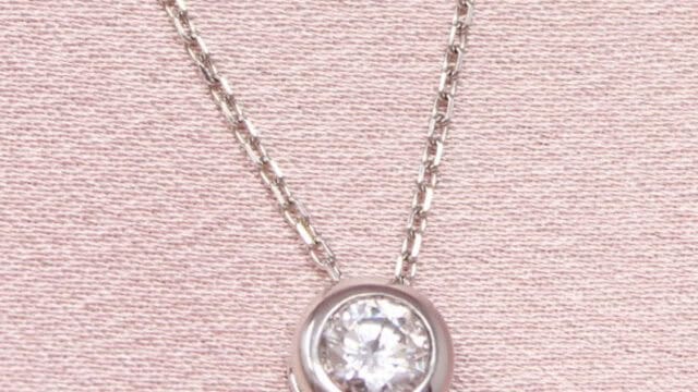 A silver chain necklace with a round diamond pendant on a light pink fabric background.