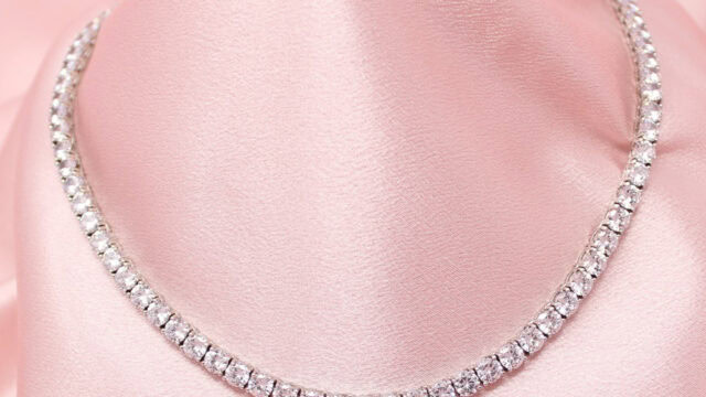 A diamond tennis necklace displayed on a pink satin fabric.